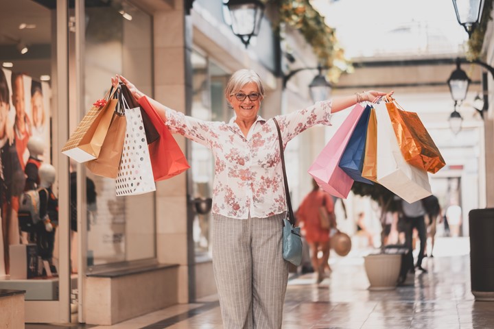 A smiling older woman holding shopping bags looking happy at camera