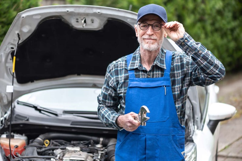 Older man in front of a car with a wrench