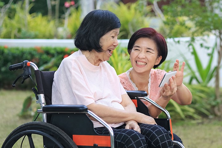 A photo of two people looking at a phone together. One person is sitting in a wheelchair.