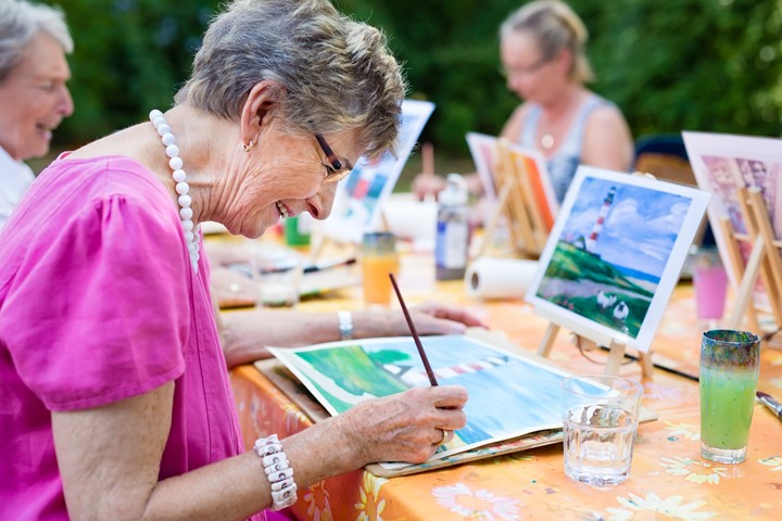 Photo of an older woman painting a picture of a lighthouse.
