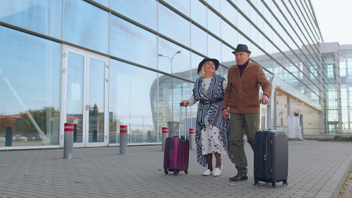 A photo of two people outside an airport walking with luggage.