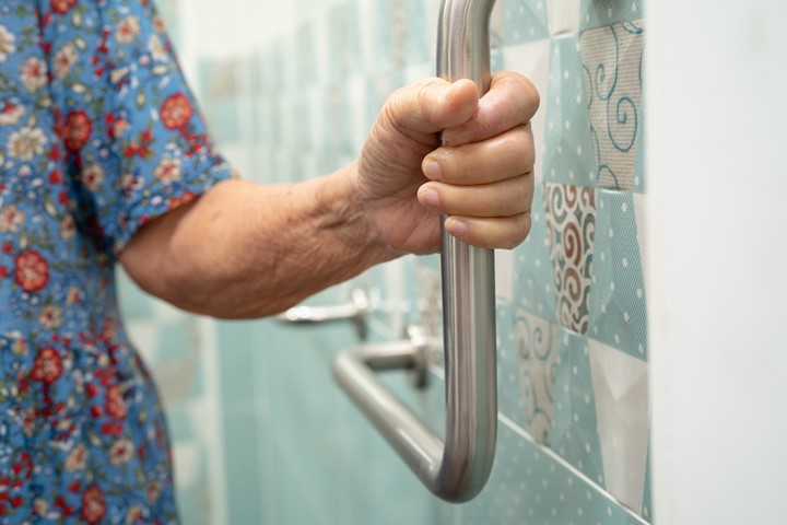 Close up of a hand holding a grab bar in a bathroom.