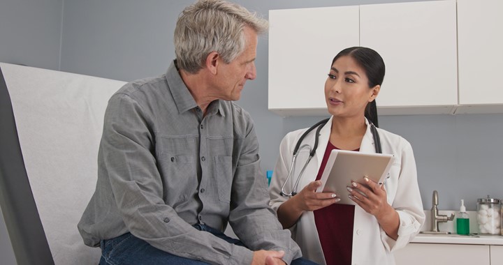 Primary care doctor explaining medical issue to senior male patient in exam room.