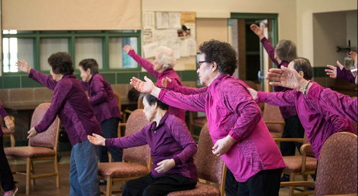 a photo of seven people stretching their arms outward in an exercise class.