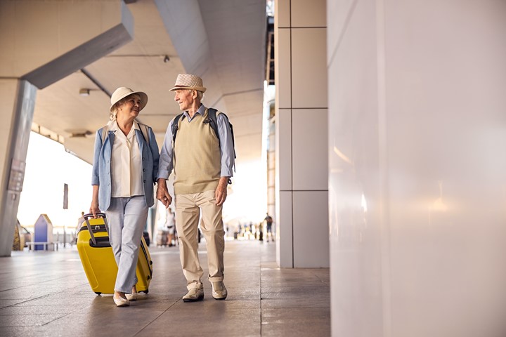Older couple walking in an airport with a suitcase.