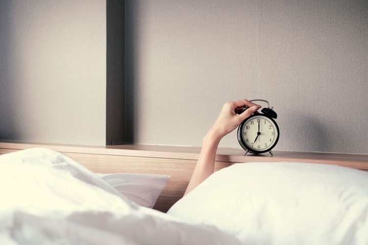 Photo of an arm reaching out of a bed to hit an alarm clock.