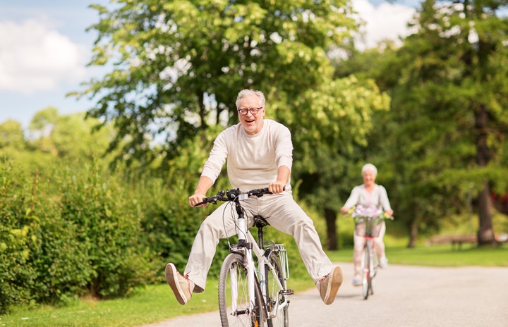 An older adult couple biking outside happily.