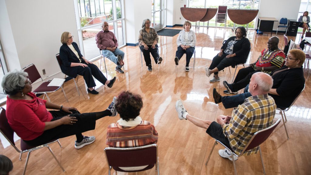 Photo of 10 people sitting in a circle with one of their legs outstretched.