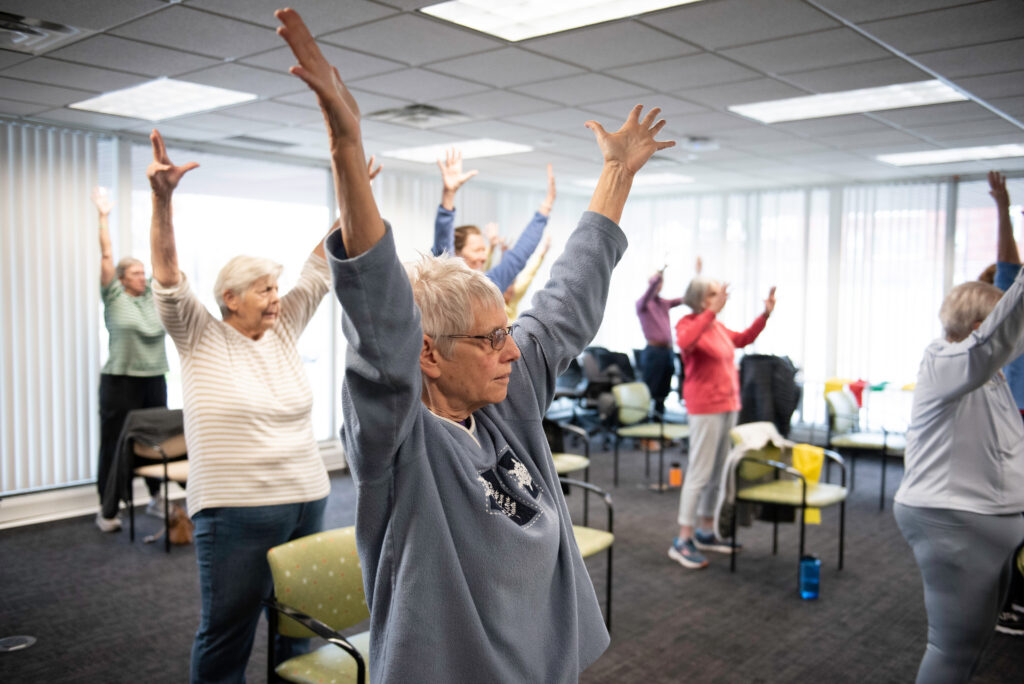 Photo of several people lifting their arms above their heads in an exercise class.