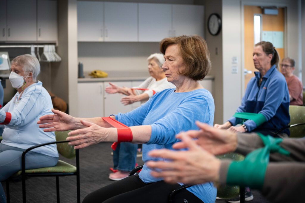Photo of several people using exercise bands on their arms while seated.