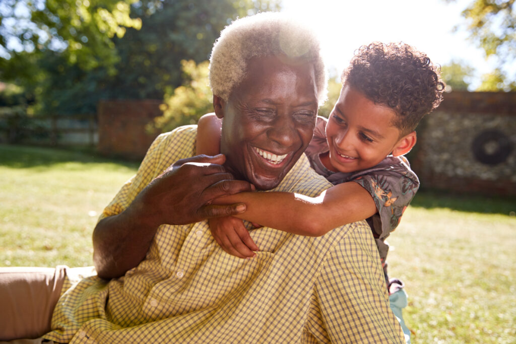 Photo of a grandparent and grandchild hugging outdoors on a sunny day.