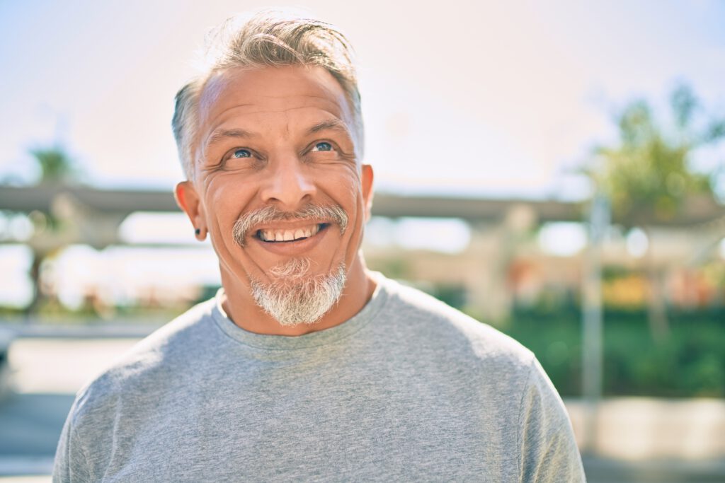 Photo of a person looking up and smiling outside on a sunny day.
