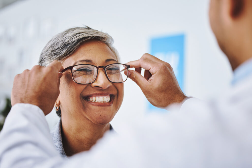 Photo of a person smiling while an optometrist puts glasses on her.