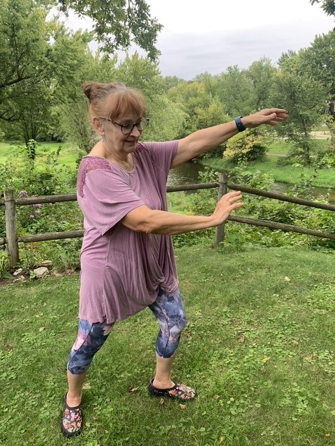 A woman standing outdoors with her arms stretched to her side.