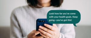 Photo of a person holding a cell phone. A text message bubble is superimposed on the image. The message reads, "Look how far you've come with your health goals. Keep going - you've got this!"